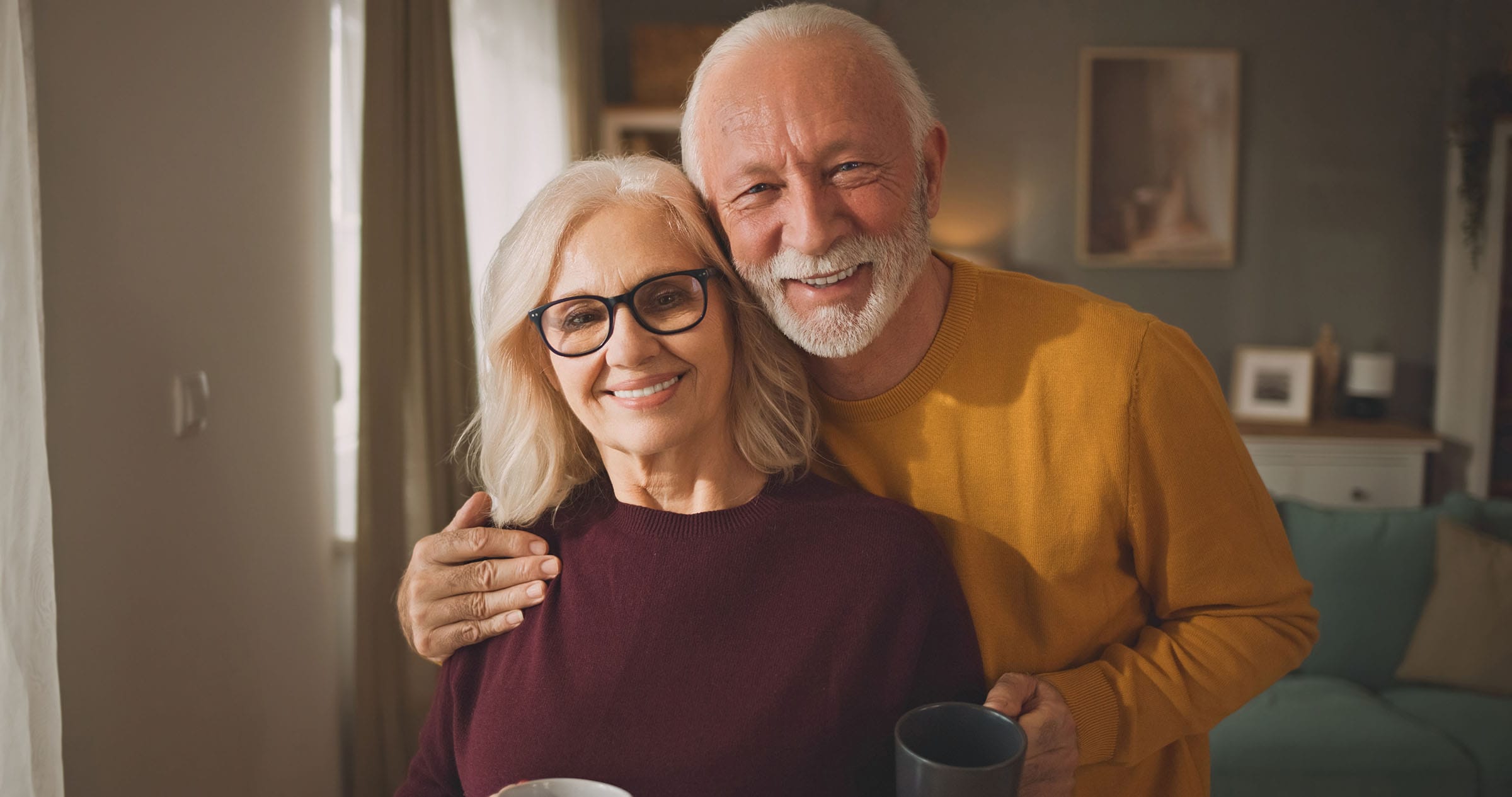 Smiling elderly couple holding mugs at home