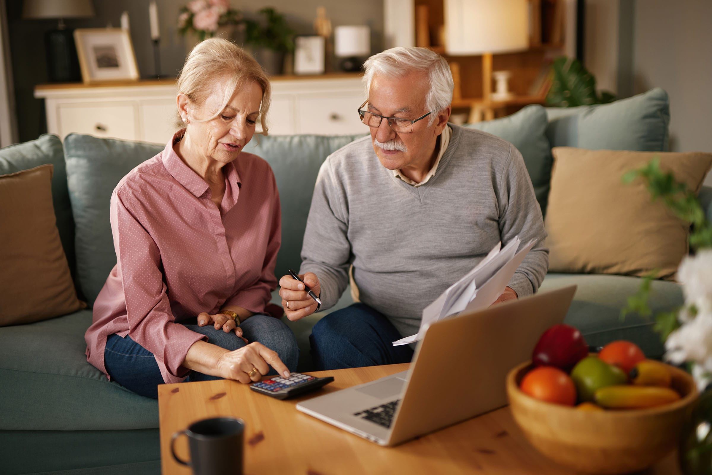Older couple reviewing bills with calculator and laptop